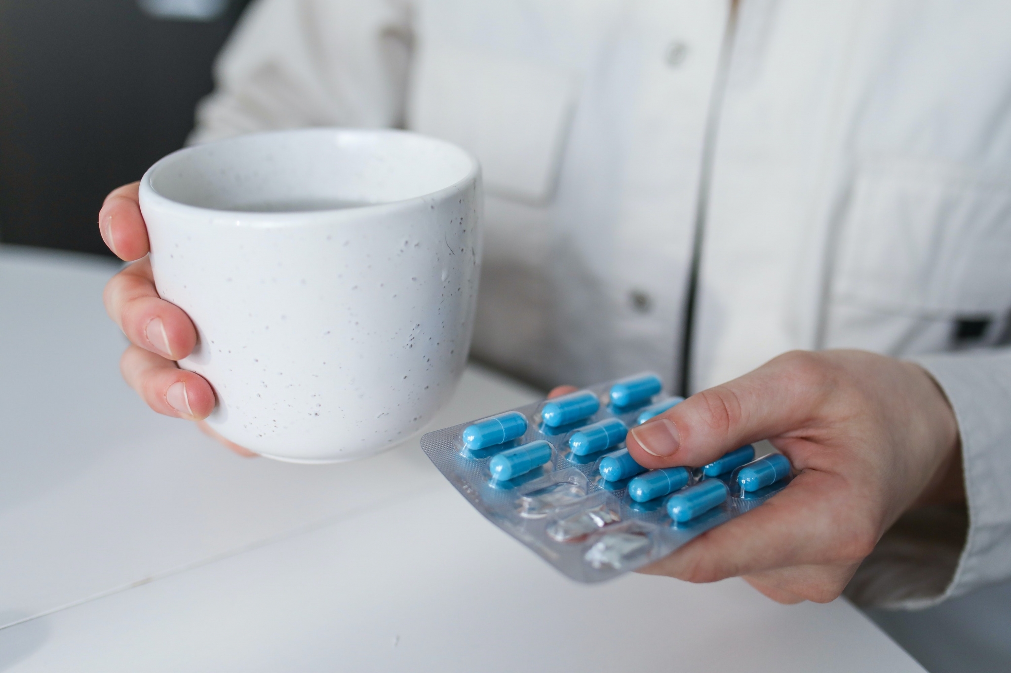 Person holding a mug and packet of pills