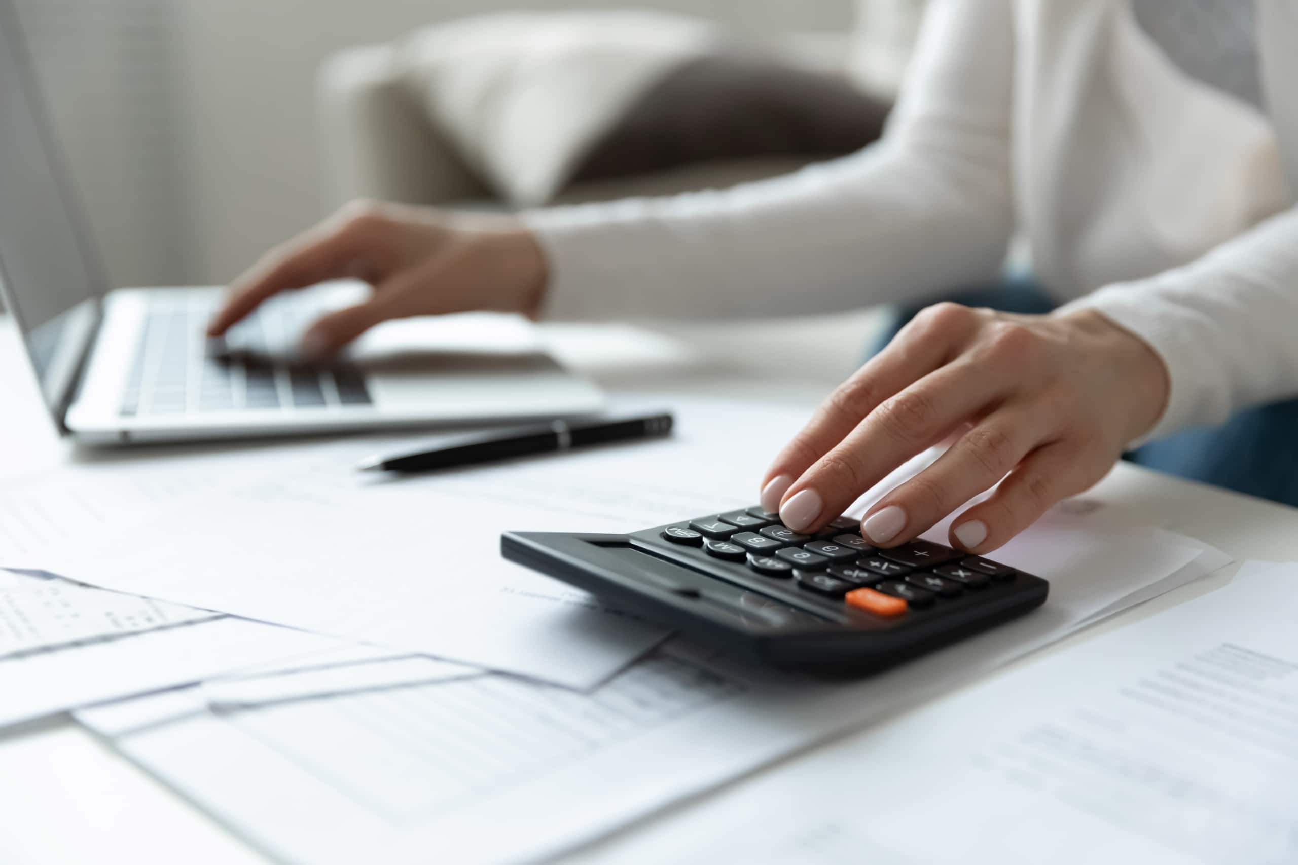 Close up of a woman using a calculator and laptop