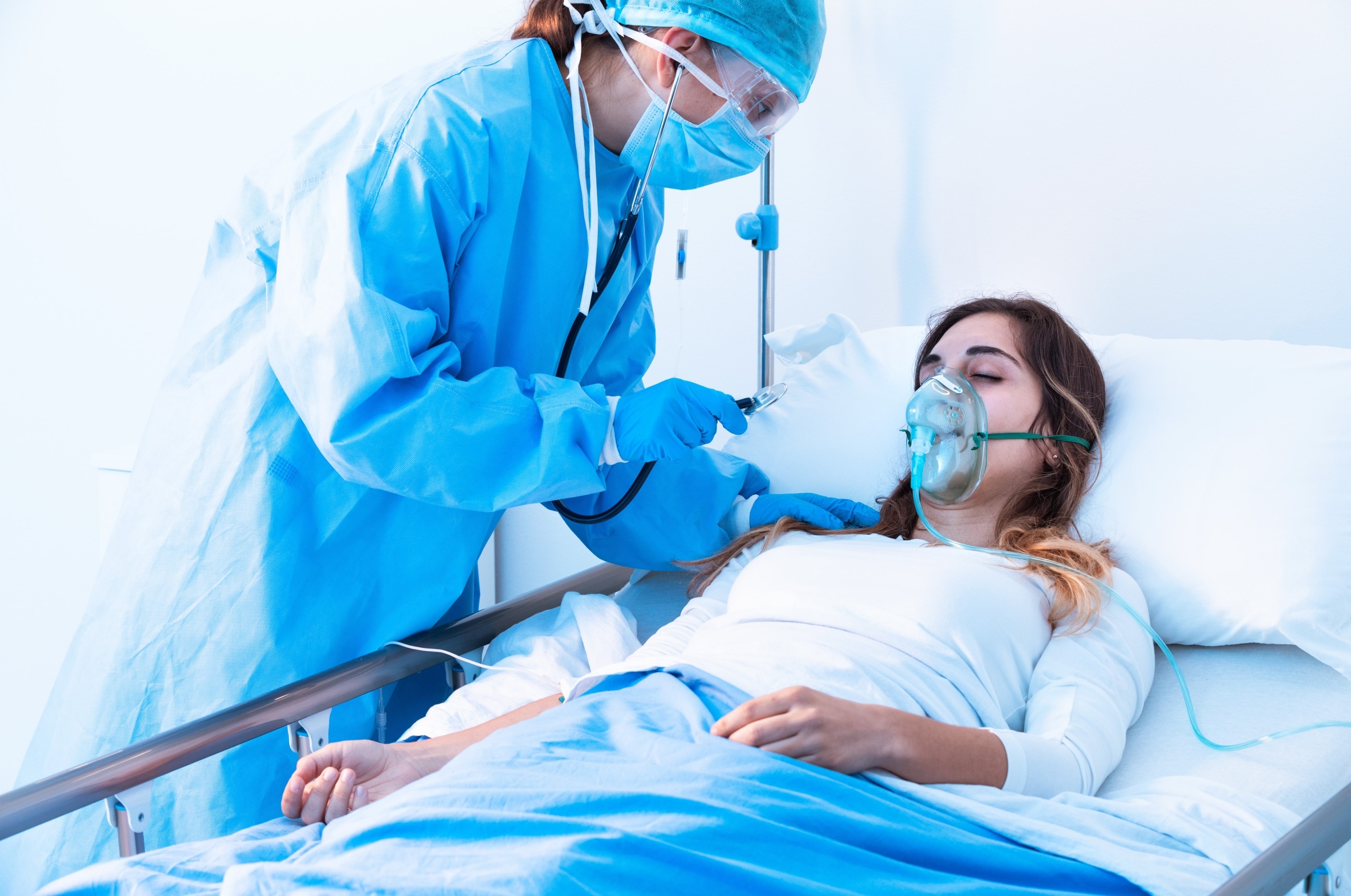 Nurse in protective gear examining a patient on oxygen