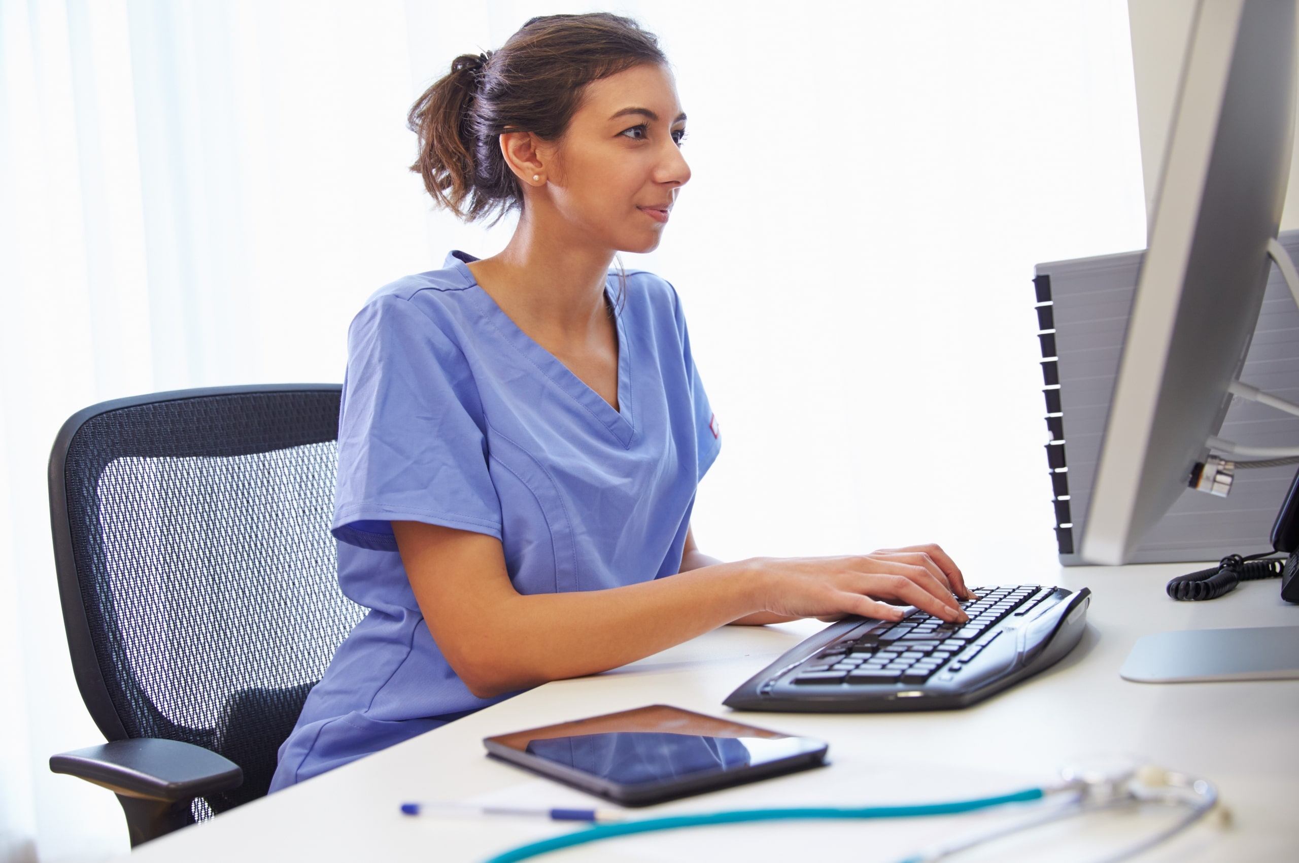 Young nurse in scrubs typing on a computer