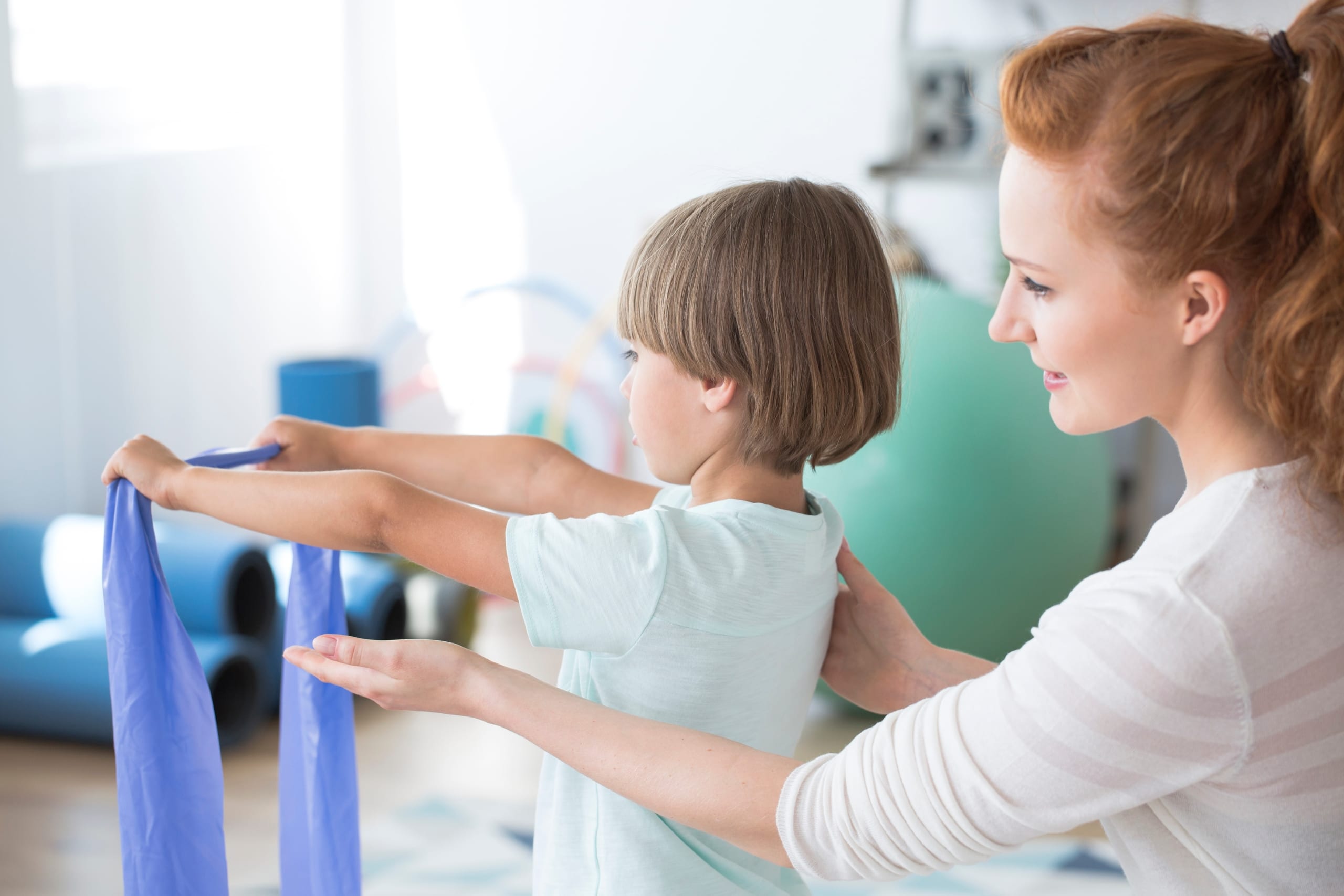 Physical therapist assistant helping a young boy use an exercise band