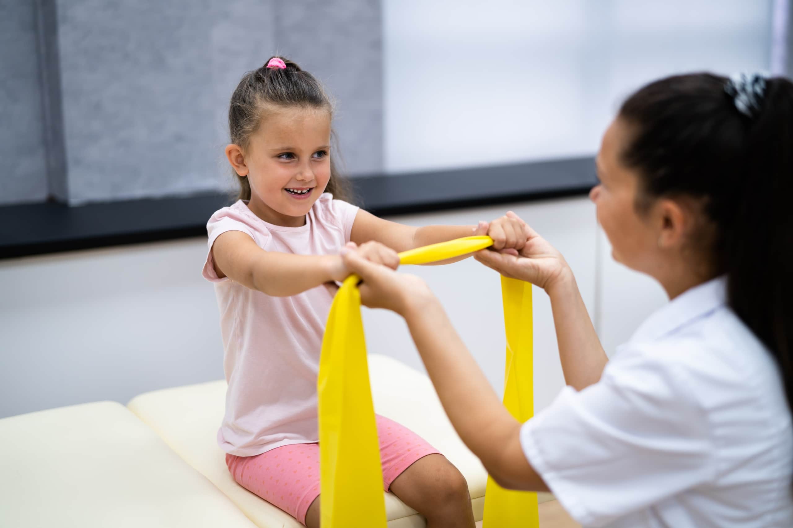 Physical therapist assistant helping a young girl use an exercise band