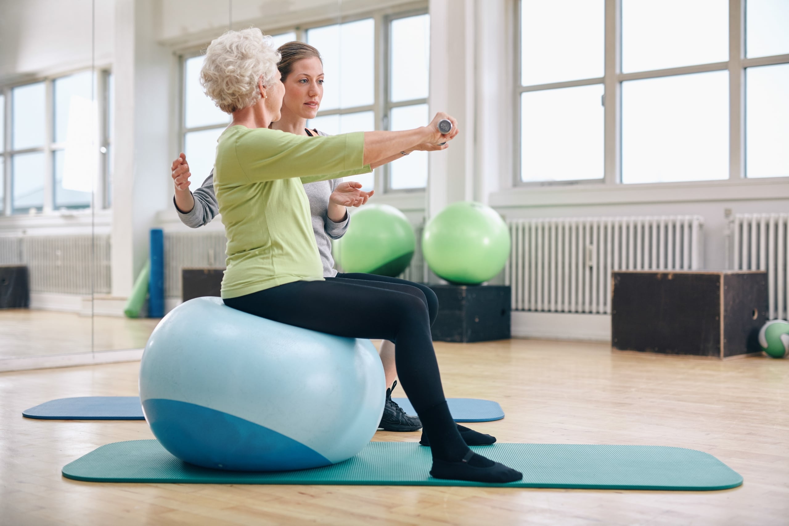 Elderly woman using an exercise ball and weights in physical therapy