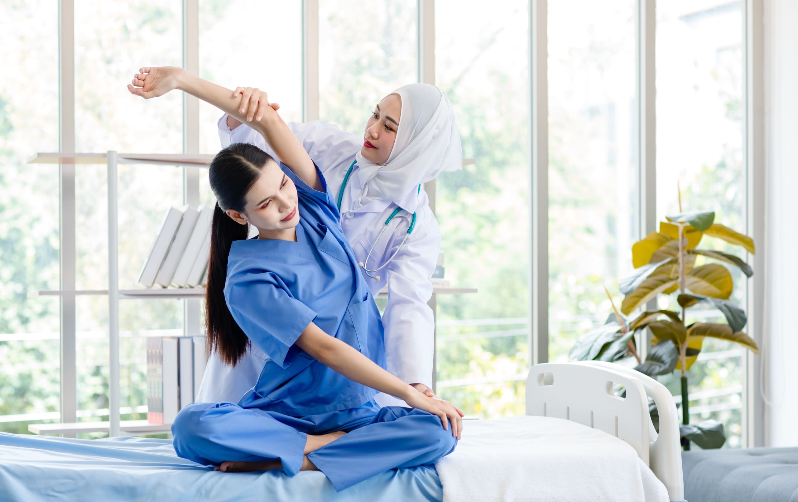 Muslim physiotherapy professional helping a woman in scrubs stretch